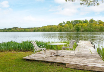 Holzterrasse mit Tisch und Stühlen am See beim 6-Personen-Ferienhaus in Bryrup, Dänemark, mit Aussicht.