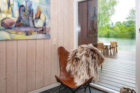 Interno di casa vacanze a Bryrup, Danimarca, con sedia in pelle, pelliccia e vista sul lago.
