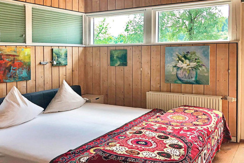 Slaapkamer met houten lambrisering, kleurrijke schilderijen en bed in vakantiehuis Bryrup, Denemarken.