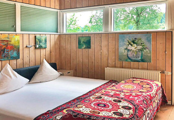 Dormitorio con paneles de madera, cuadros coloridos, ventana y cama en casa de vacaciones Bryrup, Dinamarca.