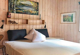 Chambre dans une maison de vacances à Bryrup, Danemark, avec murs en bois, lit double et décor artistique.