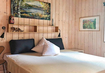 Bedroom at a holiday home in Bryrup, Denmark, with wood panel walls, double bed, art, and cozy decor.