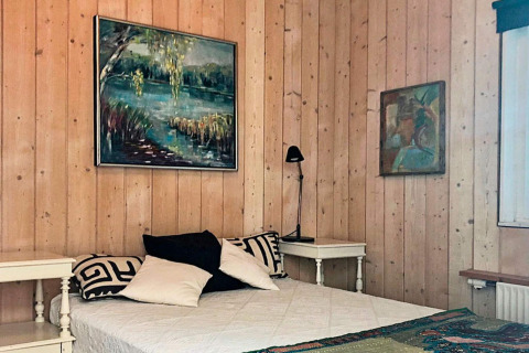 Soveværelse i feriebolig i Bryrup, Danmark med træpaneler, malerier, dobbeltseng og natborde.