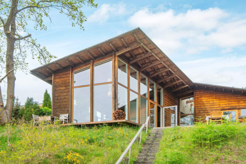 Exterior view of a wood-clad 6 person holiday home in Bryrup, featuring large windows and green lawn.
