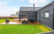 Schwarzes Ferienhaus mit Holzterrasse und grünem Rasen, 8-Personen-Lodge in Sydals, Dänemark.