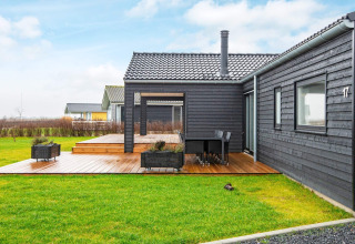 Black wooden holiday lodge with covered terrace and green lawn at 8 person holiday home in Sydals, Denmark.