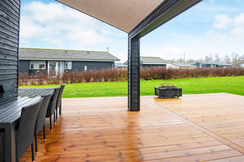 Overdækket træterrasse med spisebord og udsigt over grøn græsplæne ved et feriehus i Sydals, Danmark.
