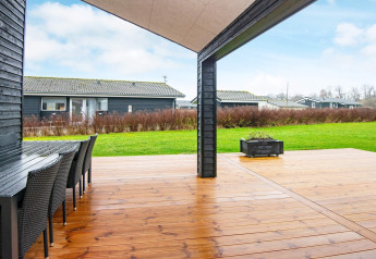 Overdekt houten terras met eettafel en uitzicht op het gazon bij een vakantiehuis in Sydals, Denemarken.