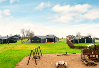 Aire de jeux et chalets noirs sur pelouse verte près d'une maison de vacances 8 personnes à Sydals, Danemark.