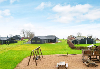 Spielplatz und schwarze Ferienhäuser auf grüner Wiese bei 8-Personen-Ferienhaus in Sydals, Dänemark.