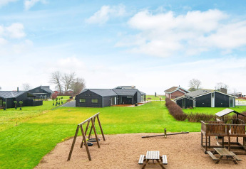 Parco giochi e chalet neri su prato verde vicino casa vacanze per 8 persone a Sydals, Danimarca.