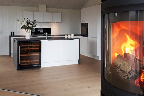 Modern kitchen in a holiday lodge with wine fridge, floral arrangement, and cozy fireplace in Sydals, Denmark.