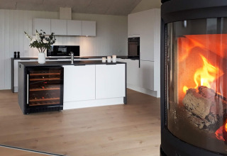 Modern kitchen in a holiday lodge with wine fridge, floral arrangement, and cozy fireplace in Sydals, Denmark.
