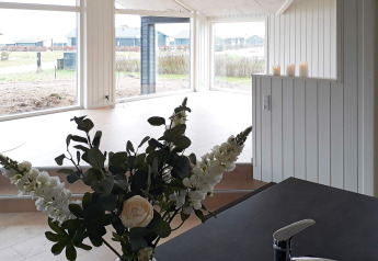 Vista interna di casa vacanze per 8 persone a Sydals, Danimarca, con fiori, candele e grandi finestre.