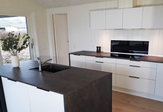 Cucina moderna in una casa vacanze per 8 persone a Sydals, Danimarca, con mobili bianchi e piano scuro.