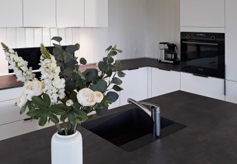 Modernes Ferienhaus-Küche in Sydals, Dänemark, mit dunkler Arbeitsplatte, Spüle und Blumen.