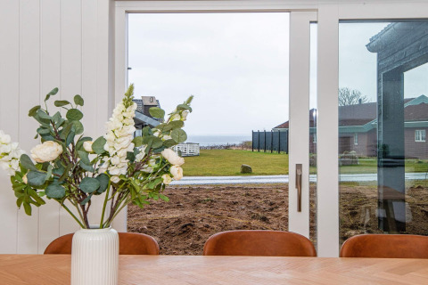 Zicht vanuit eetkamer in vakantiehuis in Sydals, Denemarken, met bloemenvaas en zee op de achtergrond.