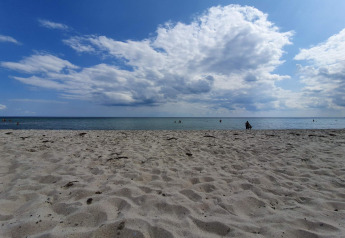 Strandblick vom 8-Personen-Ferienhaus in Sydals, Dänemark, mit Sand, Meer und bewölktem Himmel.