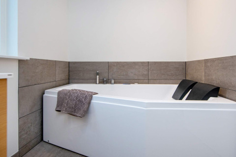 Baignoire d’angle moderne avec carrelage gris et deux appuis-tête noirs dans un gîte à Sydals, Danemark.