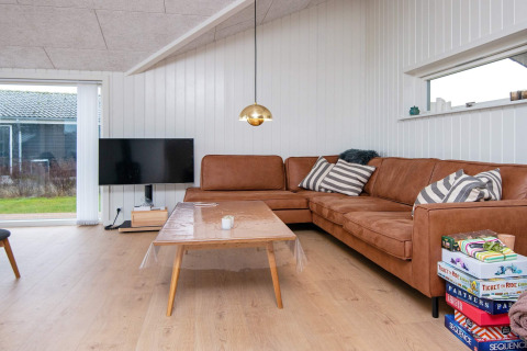 Stue i 8-personers feriehus i Sydals, Danmark, med brun sofa, TV, sofabord og brætspil på gulvet.