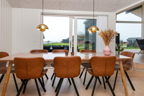 Eetkamer met acht lederen stoelen, houten tafel, en grote ramen in een vakantiehuis in Sydals, Denemarken.