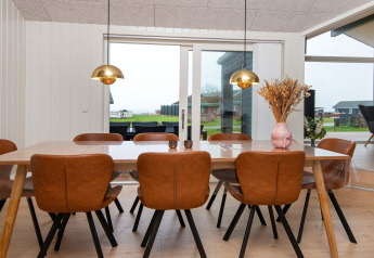 Esszimmer mit acht Lederstühlen, Holztisch und großen Fenstern in einem Ferienhaus in Sydals, Dänemark.