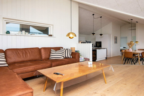 Modernes Wohnzimmer in einer Ferienwohnung mit Ledersofa, Holztisch und Blick auf die Küche in Sydals.