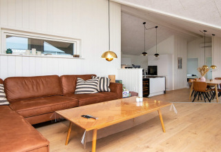 Modern living room in a holiday home with brown leather sofa, wood table and kitchen view in Sydals, Denmark.