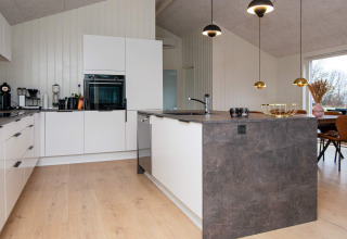 Cuisine moderne avec armoires blanches et îlot central dans une maison de vacances à Sydals, Danemark.