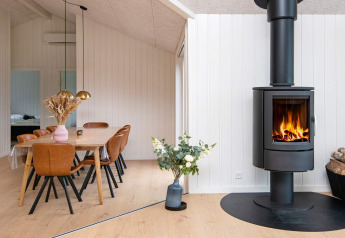Sala da pranzo moderna con stufa a legna, sedie in pelle e fiori in una casa vacanze a Sydals, Danimarca.