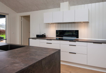 Moderne keuken in een vakantiehuis in Sydals, Denemarken, met witte kasten en donkere werkbladen.