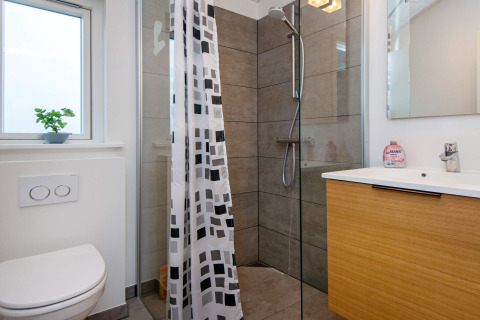 Salle de bain moderne avec douche, toilettes, fenêtre et meuble en bois dans maison de vacances à Sydals, Danemark.