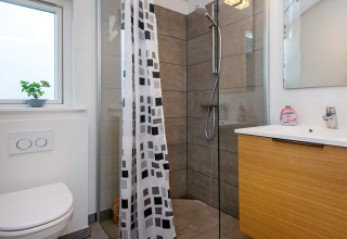 Baño moderno con ducha, inodoro, ventana y lavabo de madera en casa de vacaciones para 8 personas en Sydals, Dinamarca.