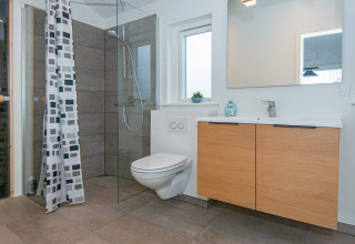 Bagno moderno in casa vacanze per 8 persone a Sydals, Danimarca, con doccia in vetro e mobile in legno.