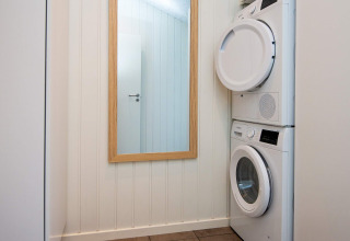 Laundry room in holiday home in Sydals, Denmark, featuring stacked washer and dryer next to a mirror.