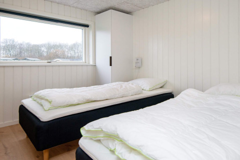 Lichte slaapkamer met twee enkele bedden, witte houten panelen en raam in een 8-persoons vakantiehuis in Sydals, Denemarken.