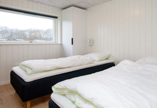 Bright bedroom with two single beds, white wooden panel walls, and window in 8 person holiday home in Sydals, Denmark.