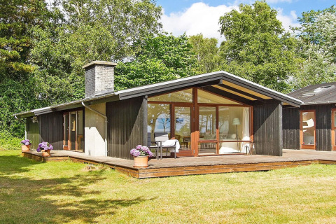 Zwarte houten vakantiewoning met grote ramen en terras, omgeven door groen in Knebel, Denemarken.