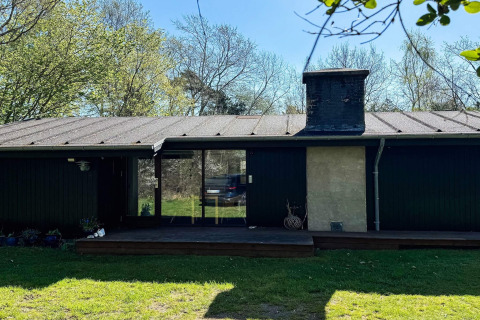 Imagen de una casa de vacaciones para 4 personas en Knebel, Dinamarca, rodeada de árboles y césped verde.