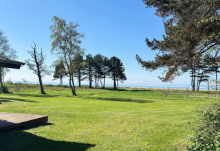 Vista da casa vacanze a Knebel, Danimarca: prato verde, alberi e mare sotto cielo limpido.