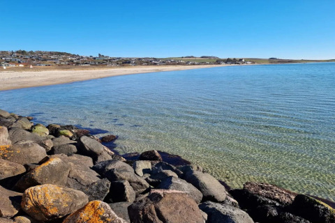 Eau claire, rivage rocheux et plage de sable à Knebel, Danemark, vue d’une maison de vacances sous ciel bleu.