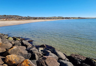 Eau claire, rivage rocheux et plage de sable à Knebel, Danemark, vue d’une maison de vacances sous ciel bleu.