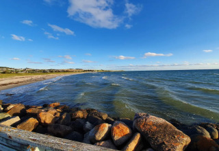Vue sur la plage et la mer depuis un chalet à Knebel, Danemark, avec des rochers au premier plan.