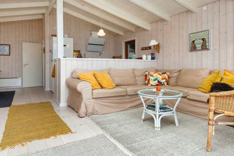 Lys stue i sommerhus i Knebel, Danmark, med beige hjørnesofa, gule puder og glasbord.