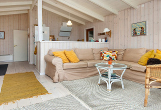 Lichte woonkamer in vakantiehuis in Knebel, Denemarken, met beige hoekbank en glazen salontafel.