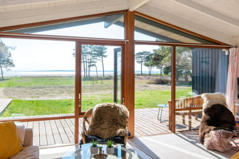 Salon d'une maison de vacances à Knebel, Danemark, grandes baies vitrées donnant sur la terrasse et la mer.