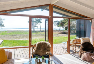 Salon d'une maison de vacances à Knebel, Danemark, grandes baies vitrées donnant sur la terrasse et la mer.