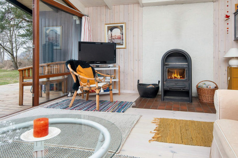 Salon d'une maison de vacances à Knebel, Danemark, poêle à bois, TV, tapis et vue sur le jardin.