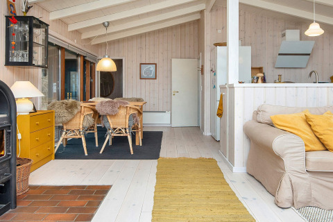Lyst, hyggeligt opholdsrum i en dansk feriehytte med trævægge, spiseplads, pejs og komfortabel sofa.
