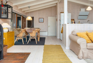 Lyst, hyggeligt opholdsrum i en dansk feriehytte med trævægge, spiseplads, pejs og komfortabel sofa.